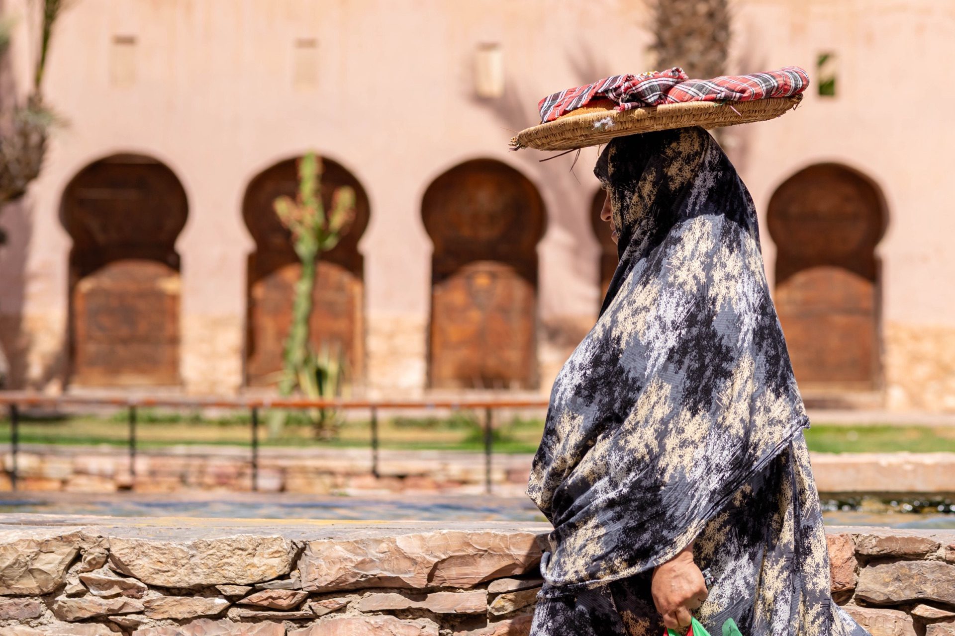 A Moroccan Amazigh woman carrying a basket on her head past a decorated doorway