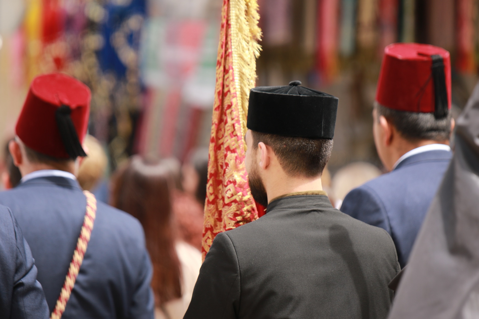 Members of an Armenian procession in red fezzes following an embroidered banner through Jerusalem
