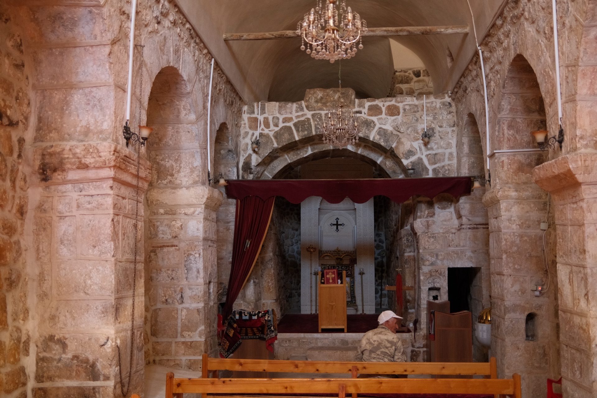 A man seated in the stone interior of the ancient church of Inwardo (Gülgöze) in Tur Abdin, Turkey