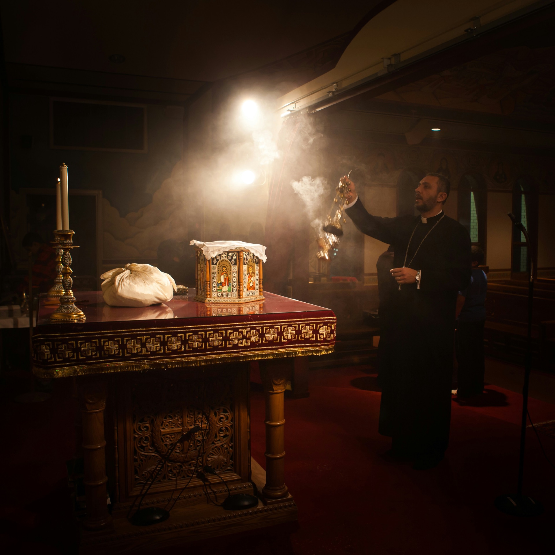 A Coptic priest swinging a censer during vespers, incense smoke curling through lamplight