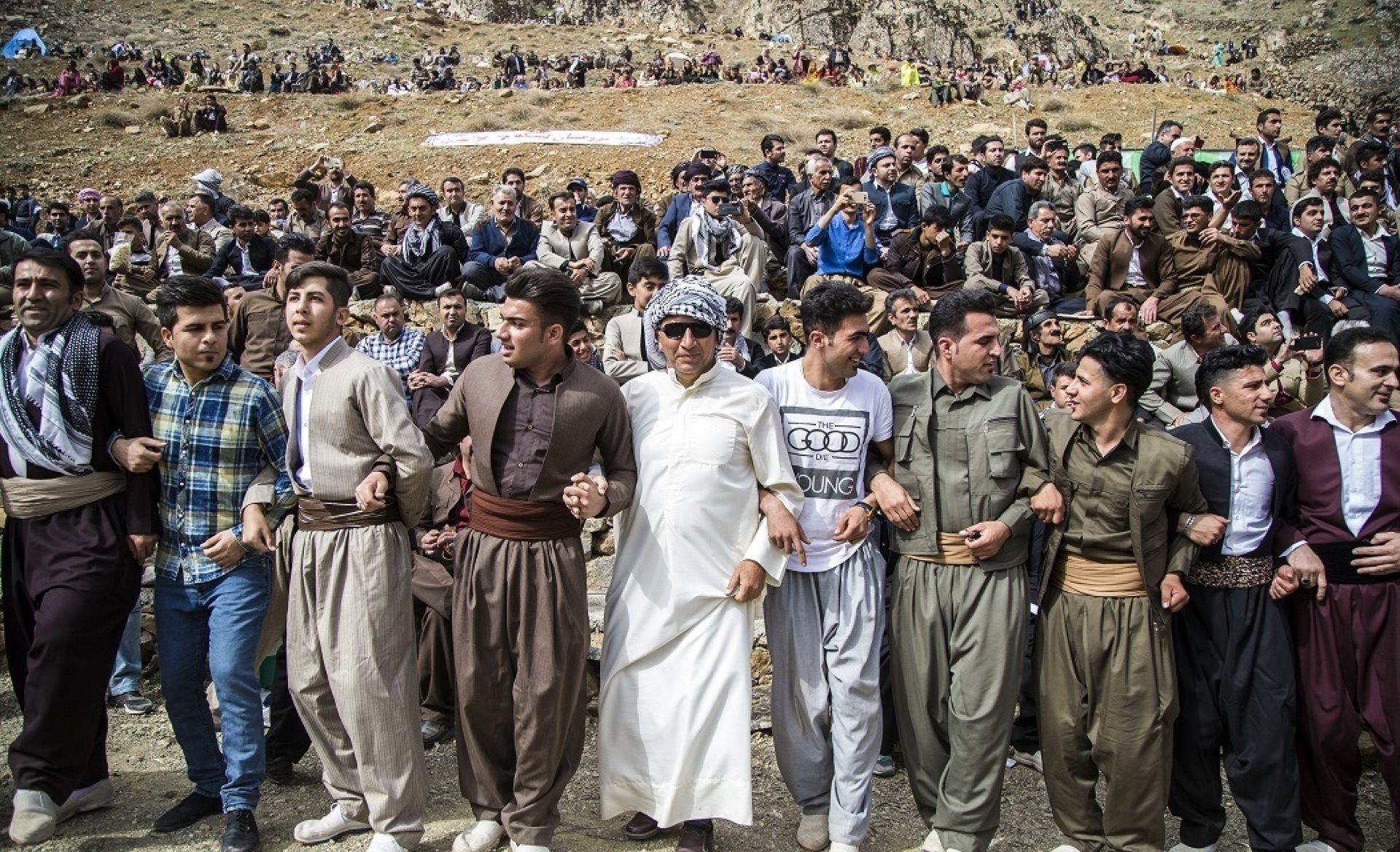 A crowd of Kurdish villagers in bright dress celebrating Newroz on a mountainside