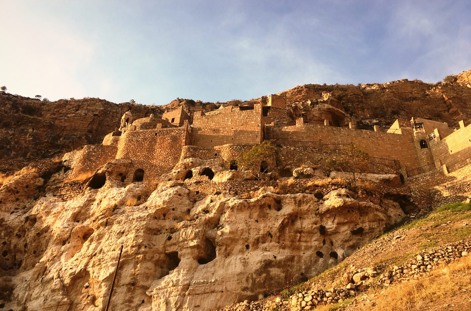 Monastic cells and ruins carved into the golden cliff face above Alqosh