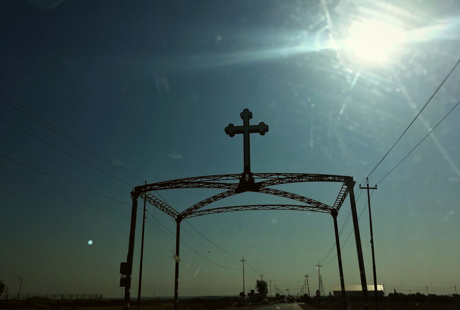 The silhouette of Alqosh's town gate, crowned with a cross, against the low sun