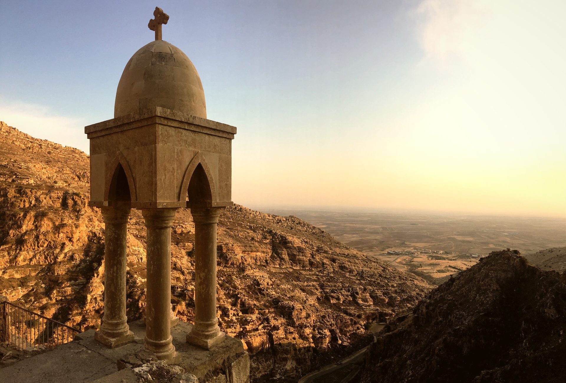 A stone bell canopy crowned with a cross at Rabban Hormizd monastery, overlooking the Nineveh plain at golden hour