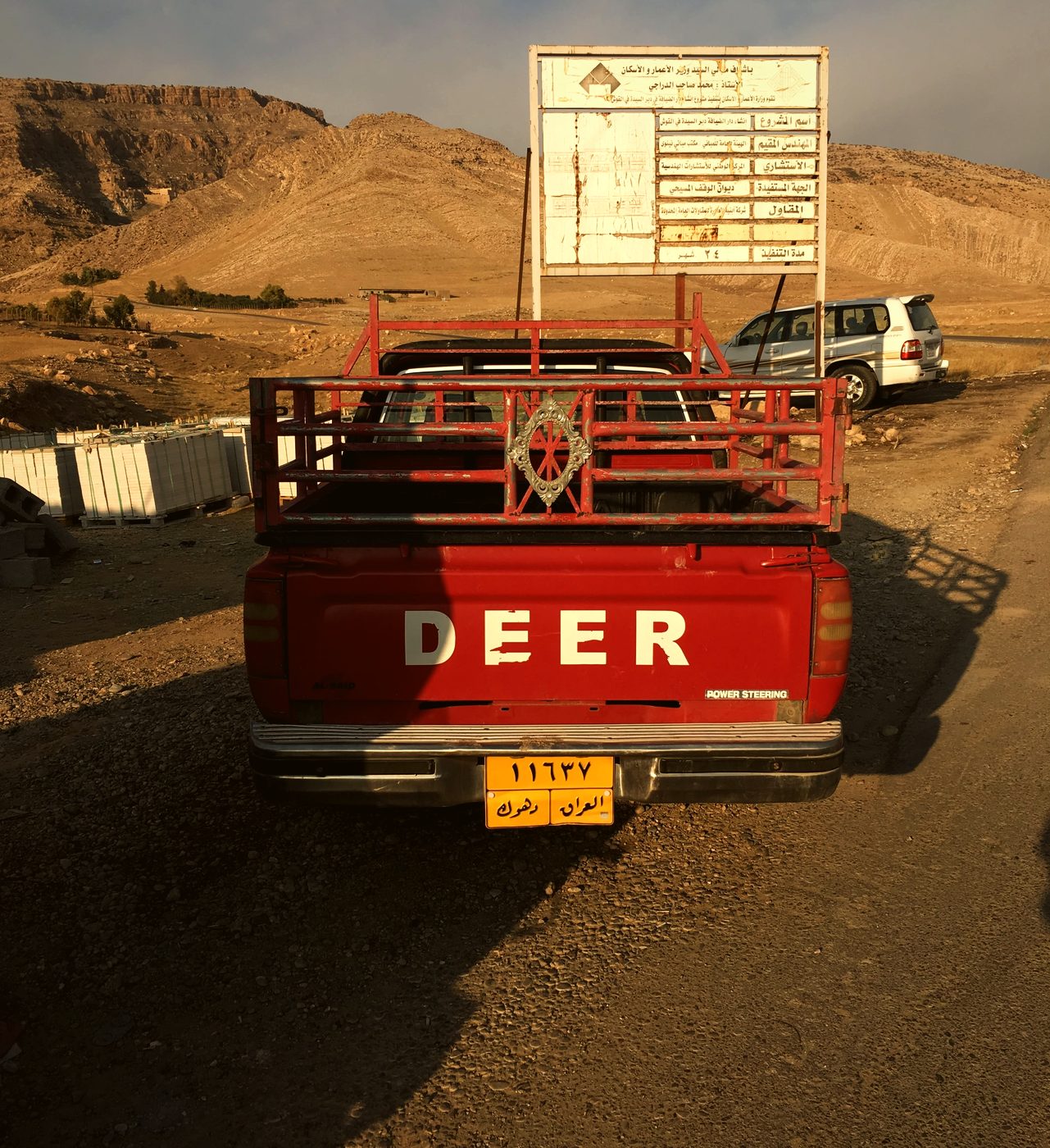 A red pickup truck marked DEER parked on a dusty track below the monastery hills