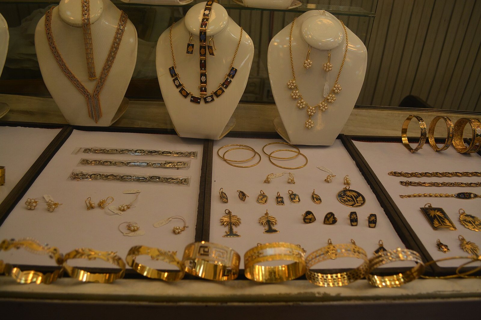 A modern Mandaean jeweller's display case, necklaces on stands and trays of gold bangles and black-inlaid pendants