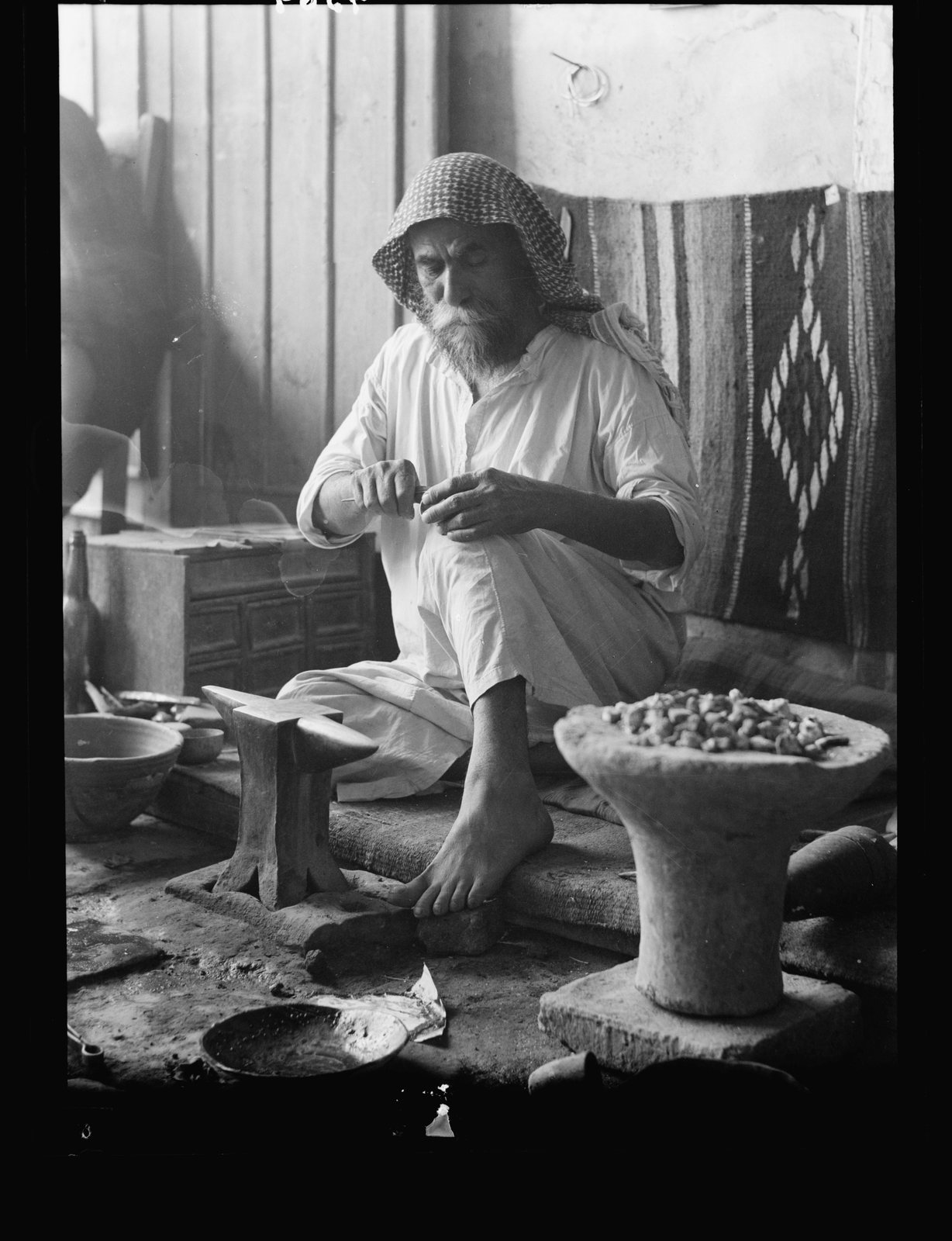 A Mandaean silversmith sitting cross-legged at a low anvil, working a small piece of silver with a graver, Baghdad, early twentieth century