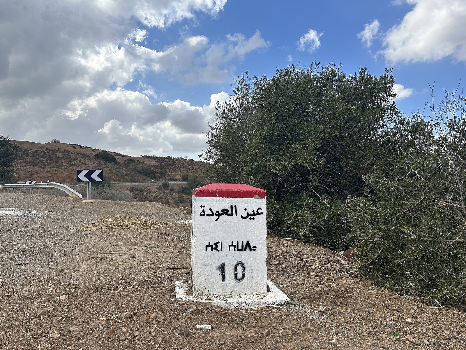 A Moroccan roadside marker painted white and red, lettered in Arabic and Tifinagh with the distance 10