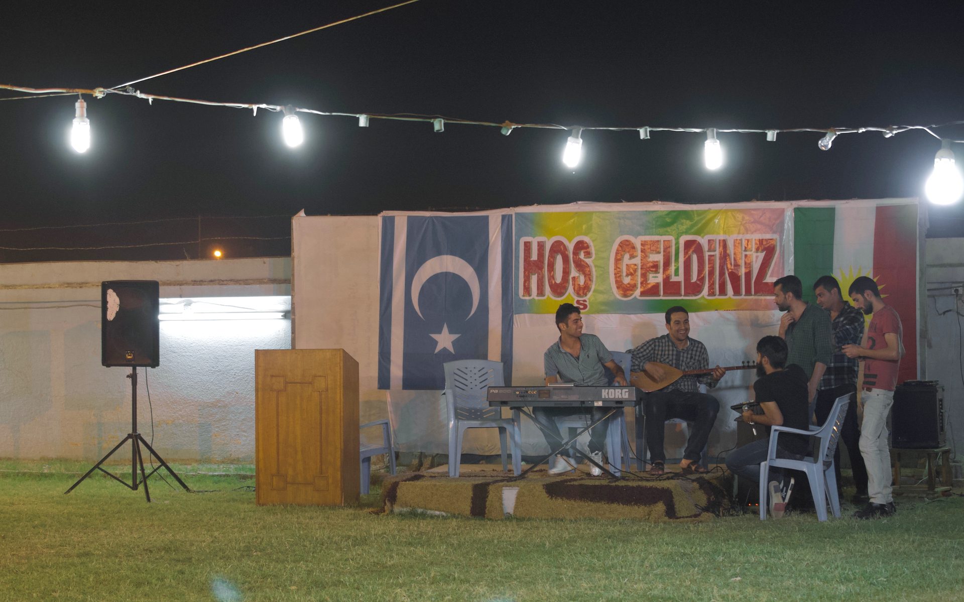 An evening gathering at the Turkoman culture centre in Erbil, with a saz player, the Iraqi Turkmen flag and a welcome banner