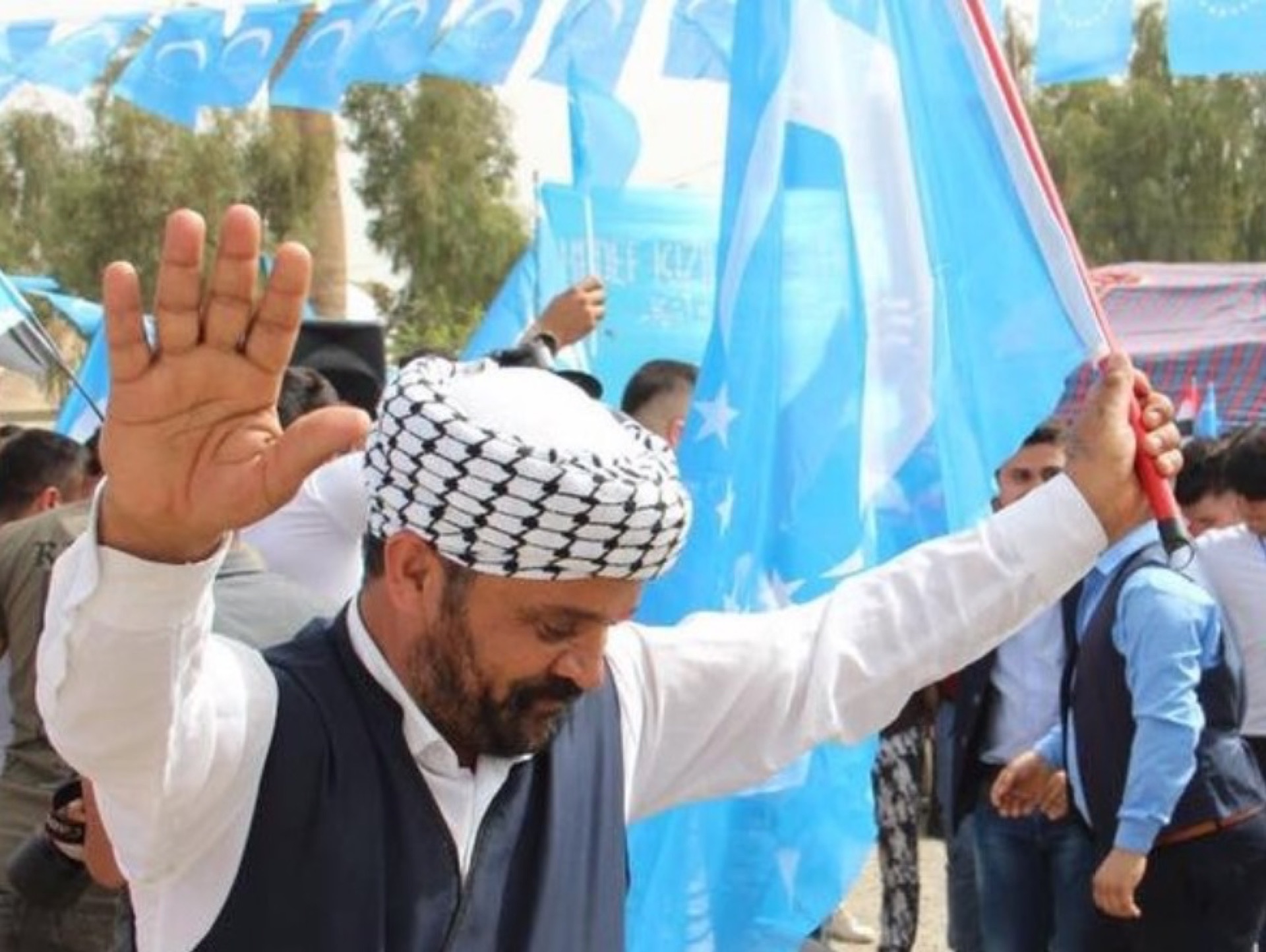 An Iraqi Turkmen man dancing with the blue crescent-and-star Turkmen flag at a rally