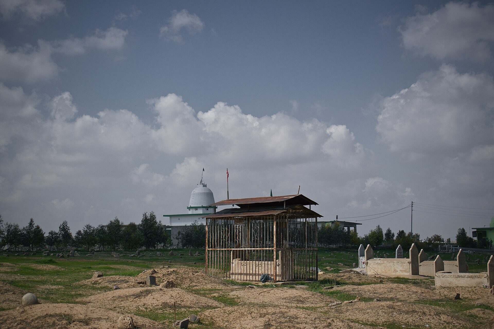 A whitewashed conical-domed Kaka'i shrine amid a village cemetery on the Nineveh plain