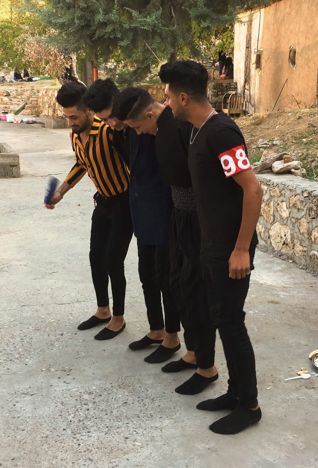 Four young Yazidi men dancing in a linked line on the paving at Lalish